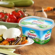 Strained yogurt container with a dish of food and vegetables on a wooden table.